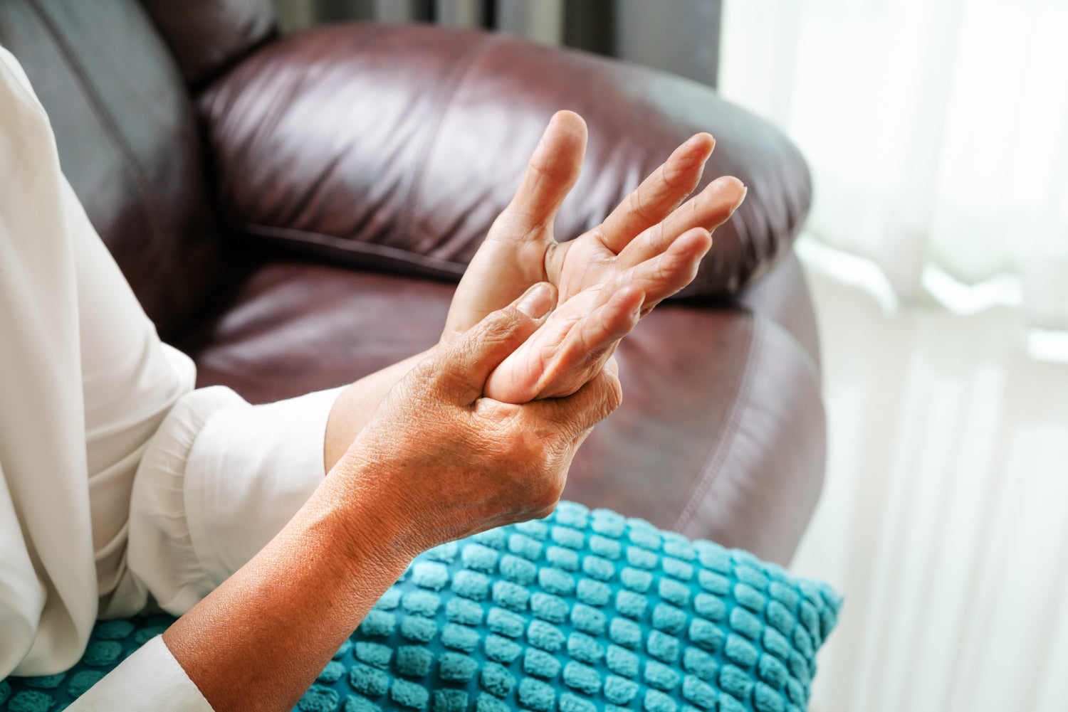 Senior woman holding and examining a trembling hand at home, illustrating what causes tremors in the elderly.
