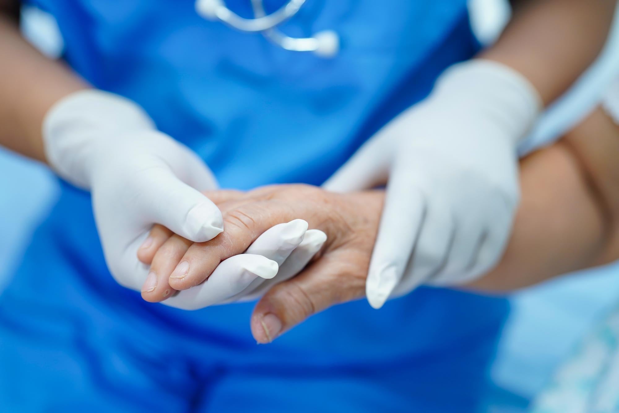 A nurse examining a patient experiencing hand tremors after surgery in a recovery room.
