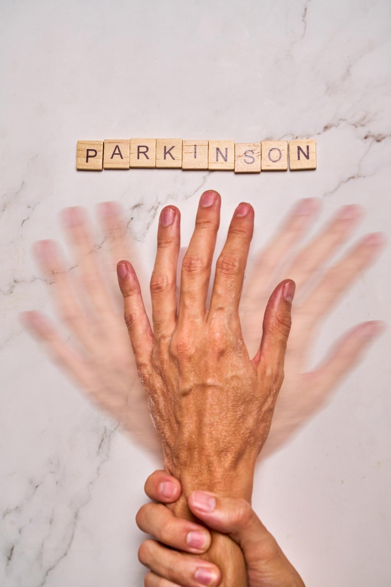 Scrabble tiles spelling Parkinson on marble surface above hands showing early warning signs of Parkinson's disease.