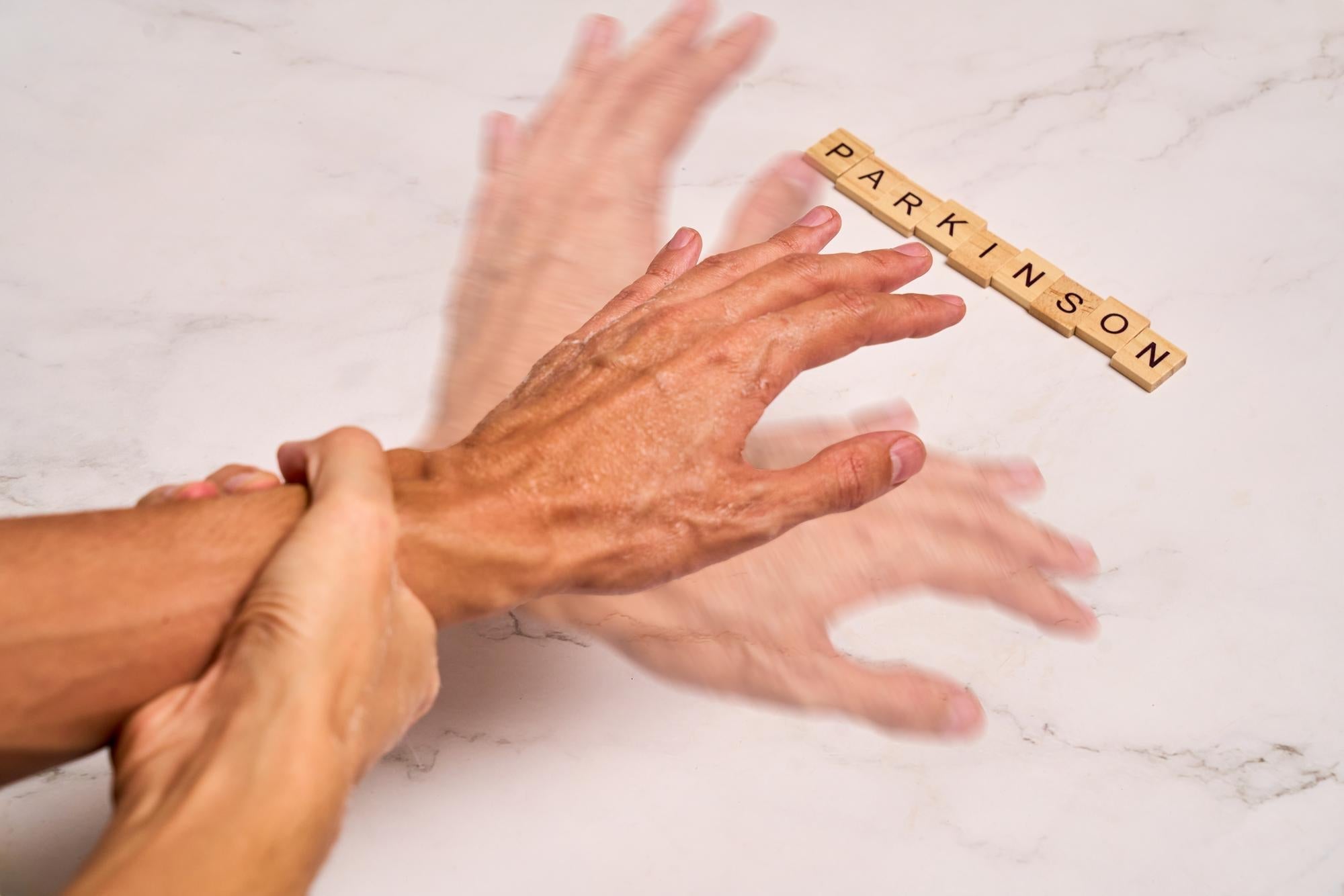 Shaking hand beside Parkinson's tiles showing the difference between Essential Tremor and Parkinson's.