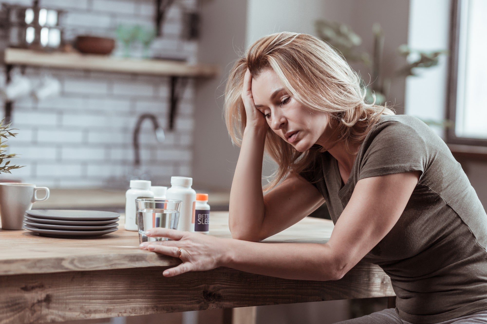 Stressed woman at a kitchen table with medication, illustrating Essential Tremor and stress as key triggers.