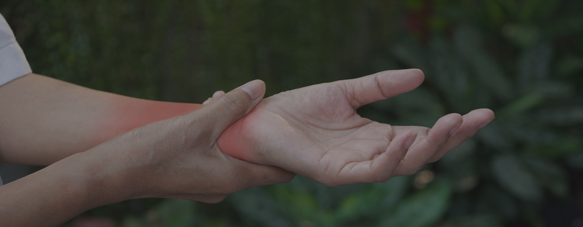 A close-up of a person's hand holding another hand's wrist, with a red heat-like glow indicating pain or discomfort, set against a blurred green outdoor background.