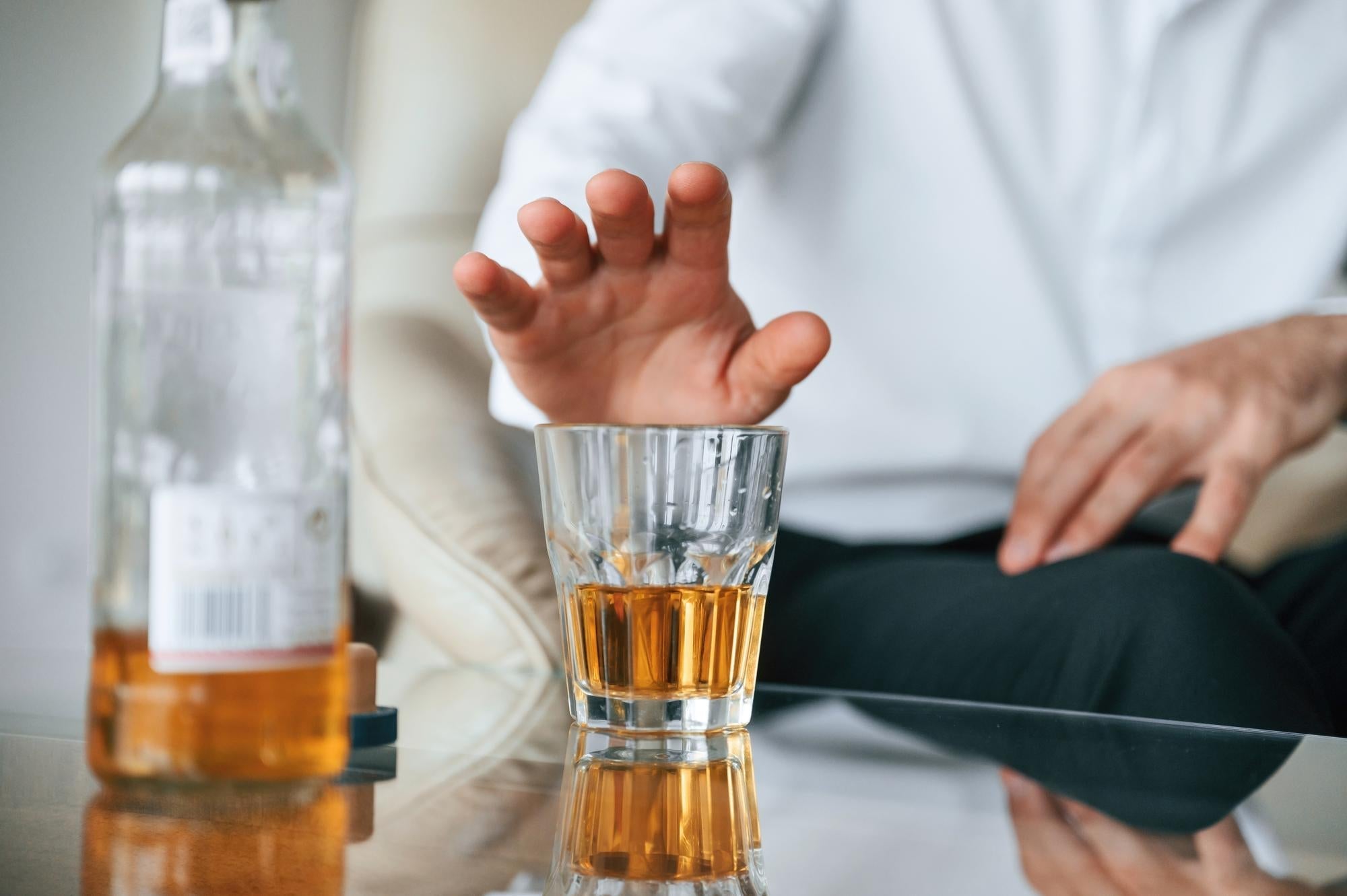 Shaking hand reaching for a whiskey glass, showing the Essential Tremor alcohol self-medication pattern.