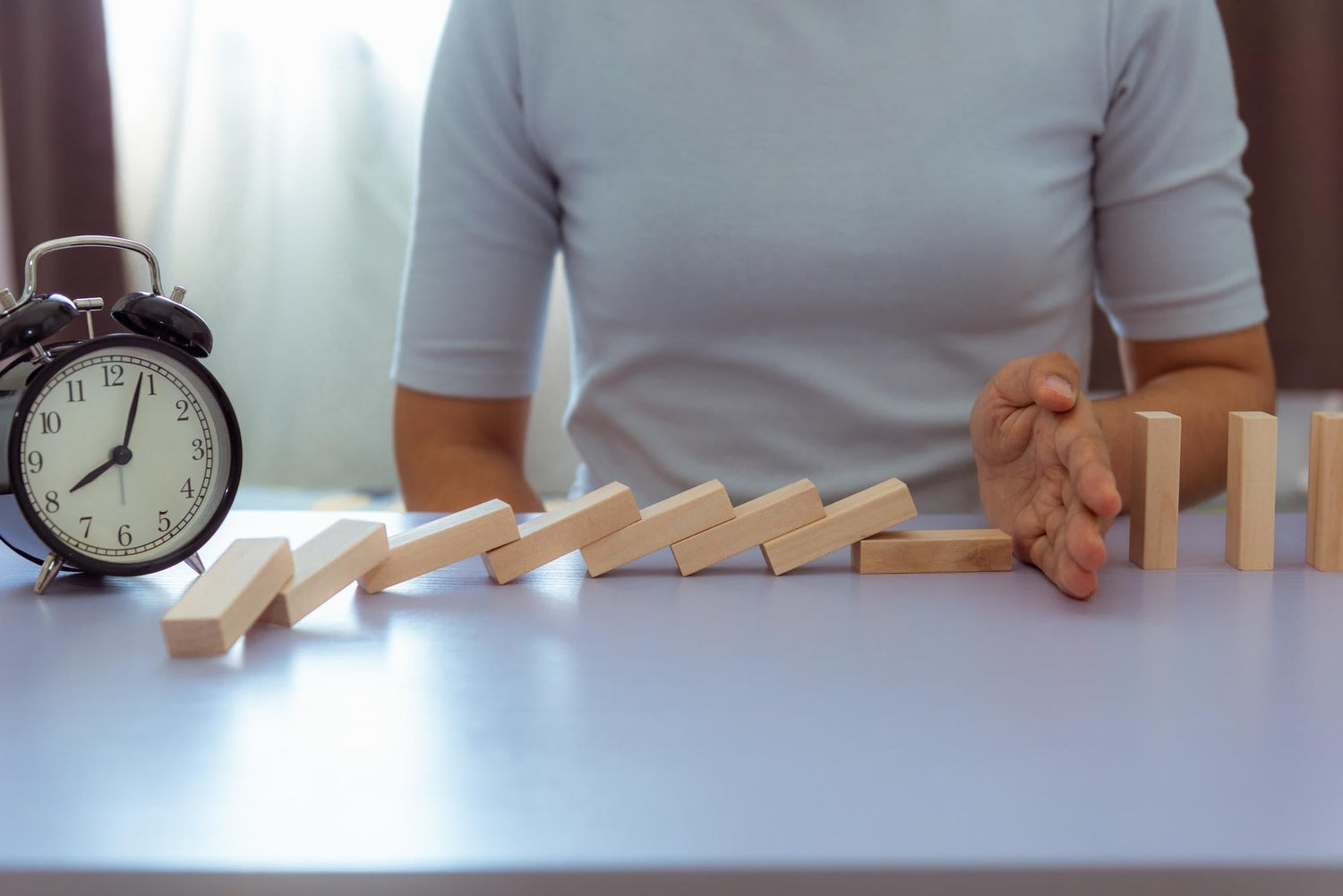 A woman’s mid-section and hands as she blocks a stack of toy wooden blocks while sitting at a table, illustrating fine motor challenge and tremor interference.