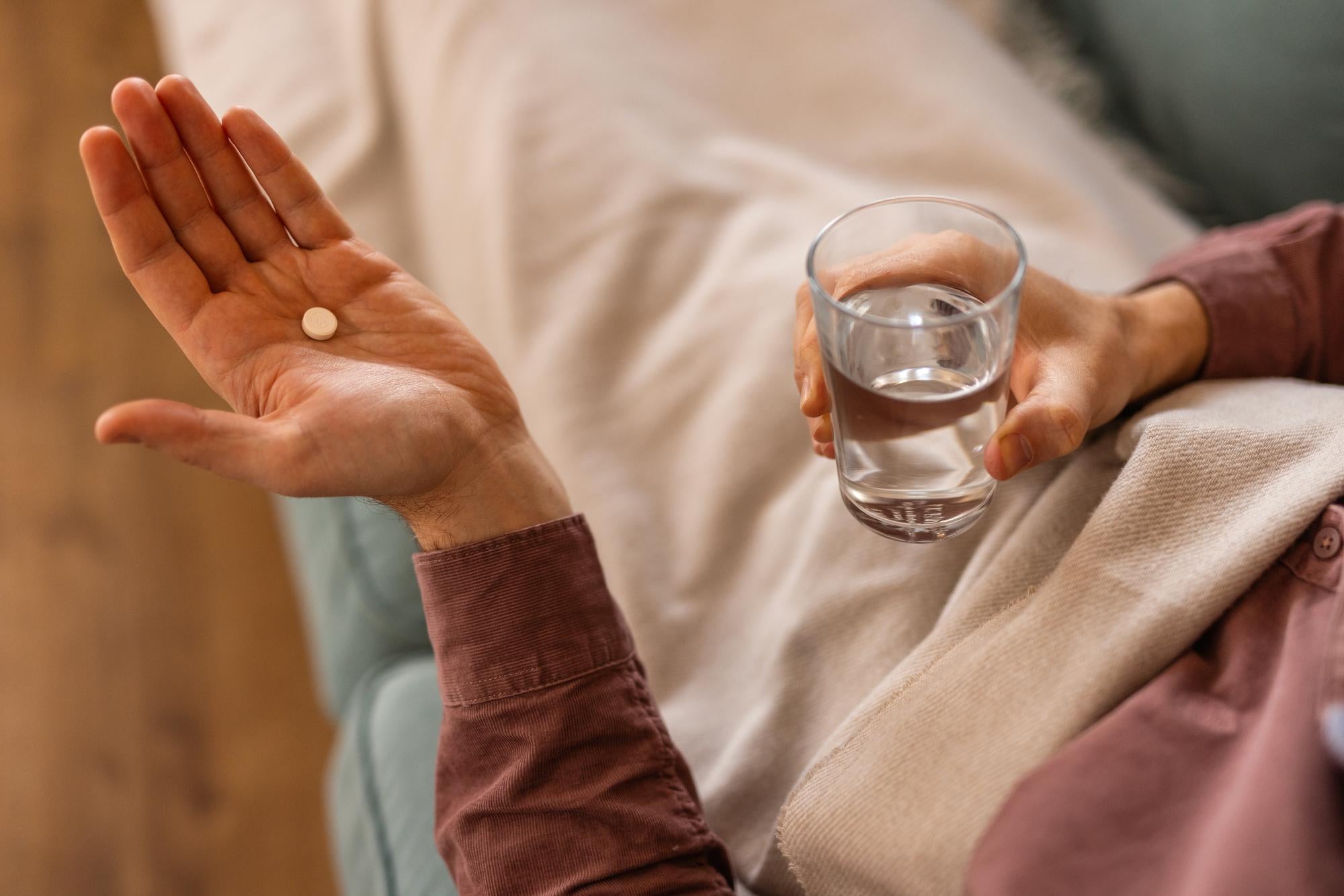 Older woman taking a vitamin supplement with water to address nutritional causes of hand tremors.
