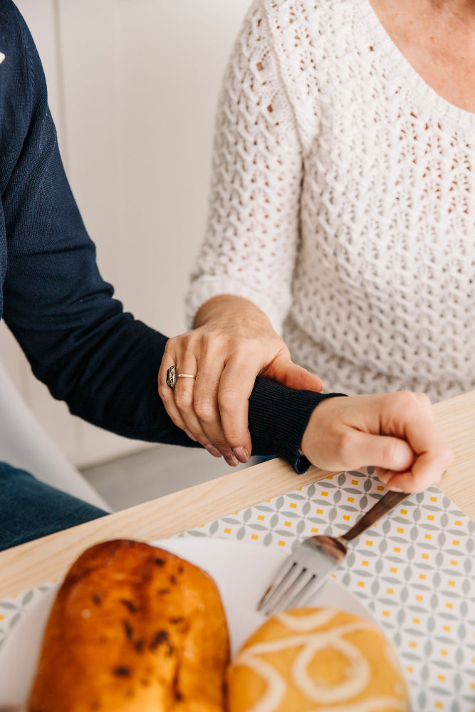  Caregiver gently supporting an older adult’s hand during mealtime, illustrating assisted eating and daily support for Essential Tremor.