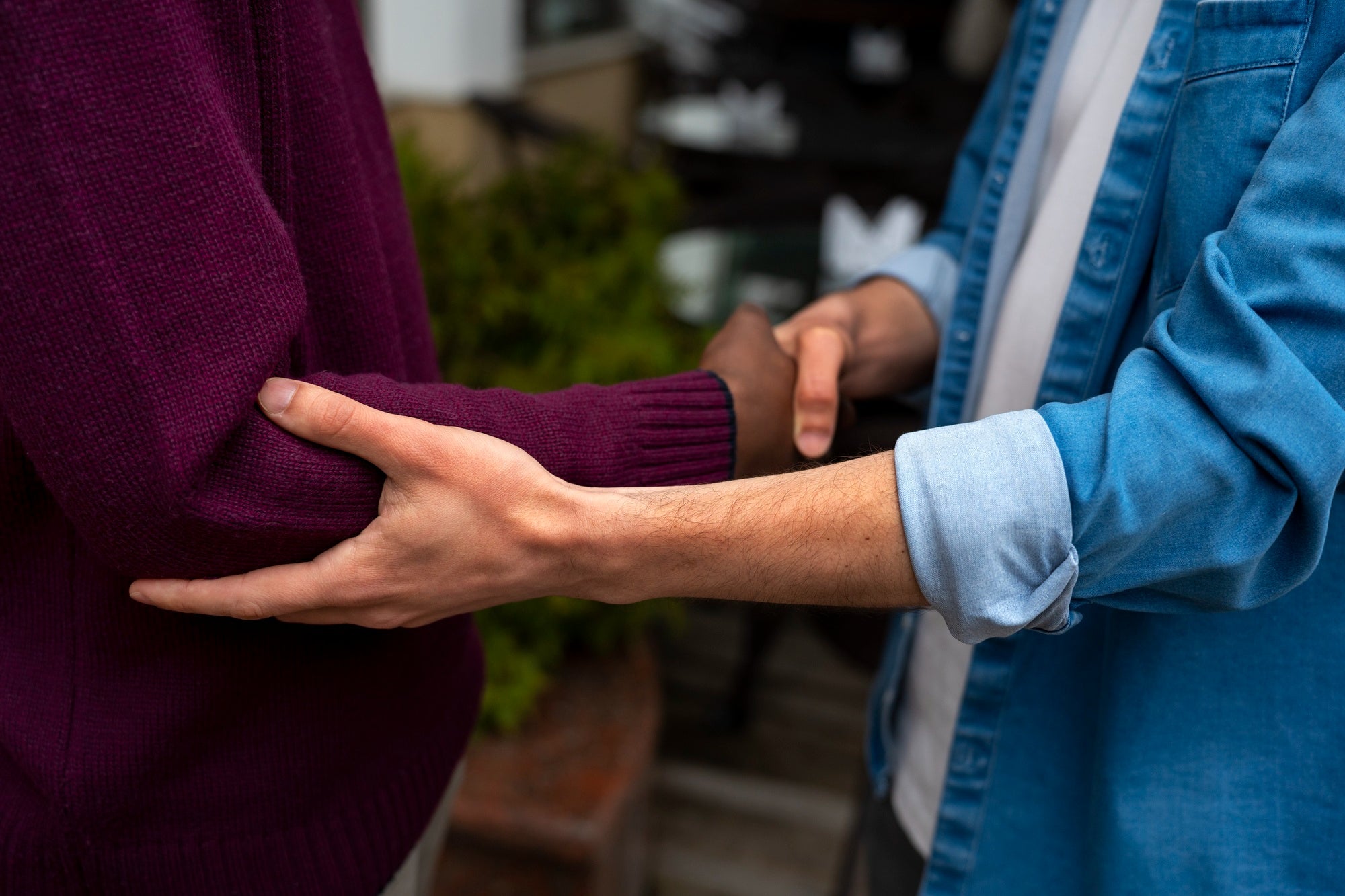 Two people shaking hands outdoors, one visibly experiencing hand tremor.