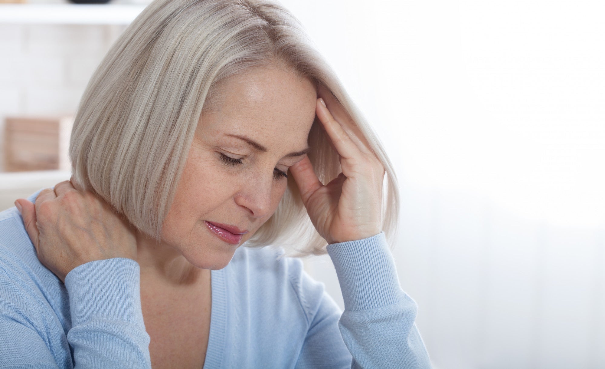 Older woman holding head and neck showing signs of Parkinson's disease in women, including pain and non-motor symptoms.