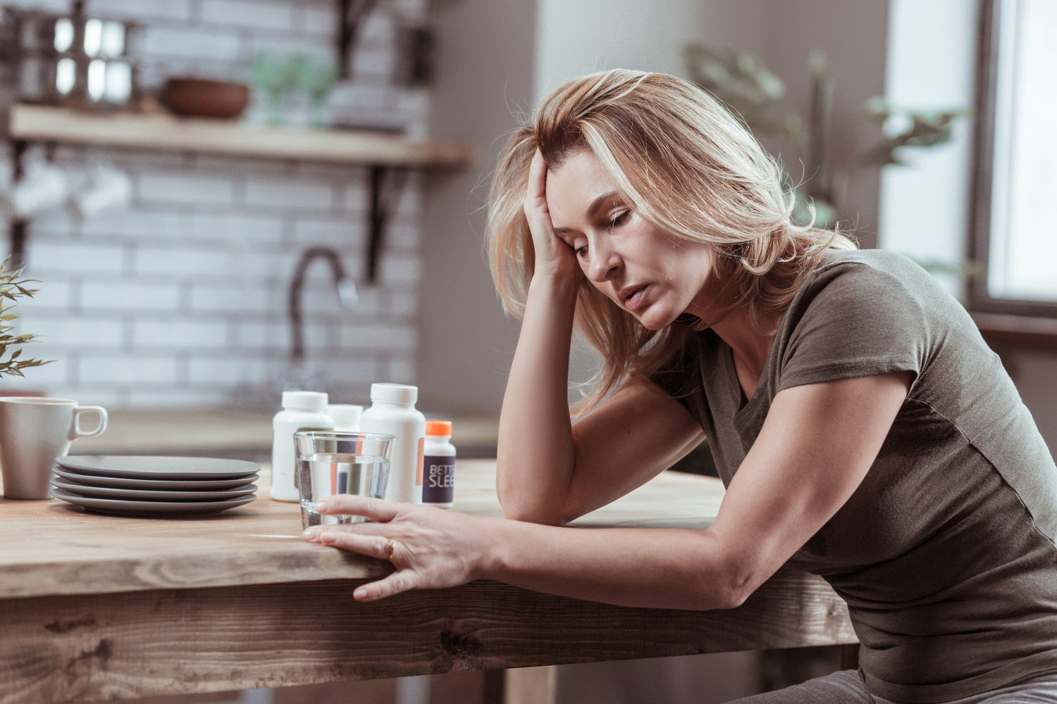 Stressed woman at a kitchen table with medication, illustrating Essential Tremor and stress as key triggers.