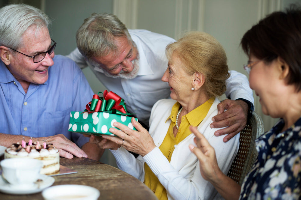 Gifts for Parkinson's patients for an older adult smiling in front of a birthday celebration cake.