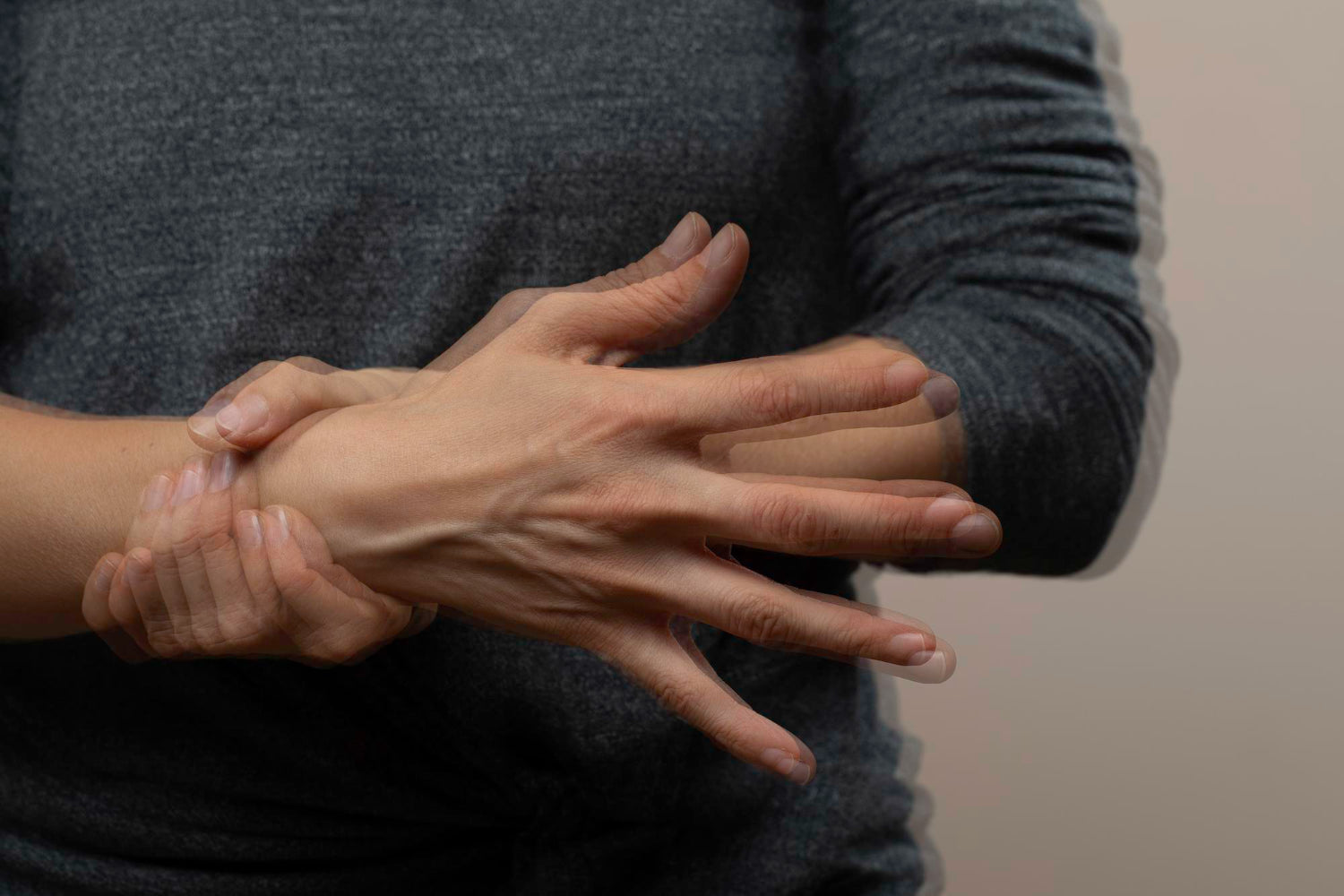 person in grey sweater gripping trembling wrist during everyday movement.