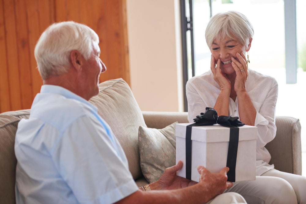 Gifts for someone with Parkinson's that an older couple on a sofa is sharing a wrapped present at home.