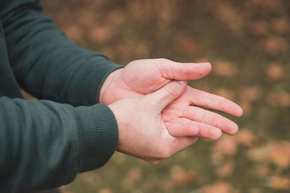 Close-up of hands with one gripping the other at the wrist outdoors, representing a self-steadying technique used to manage hand tremor symptoms.
