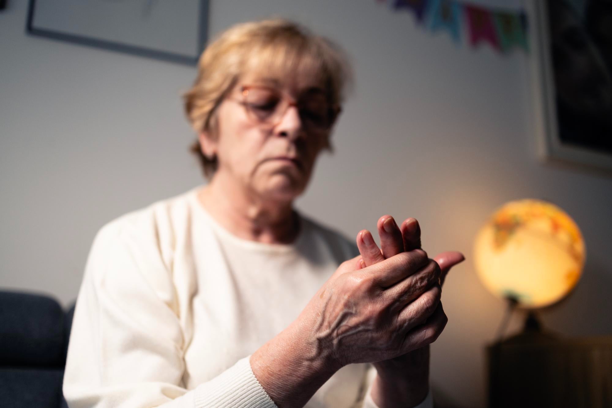 Older woman examining a trembling hand, wondering if Essential Tremor can turn into Parkinson's Disease.