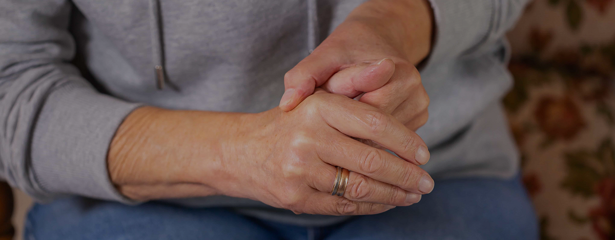 Person with a wedding ring clasping their own hands in their lap, representing the daily challenges of living with Parkinson's Disease at work.